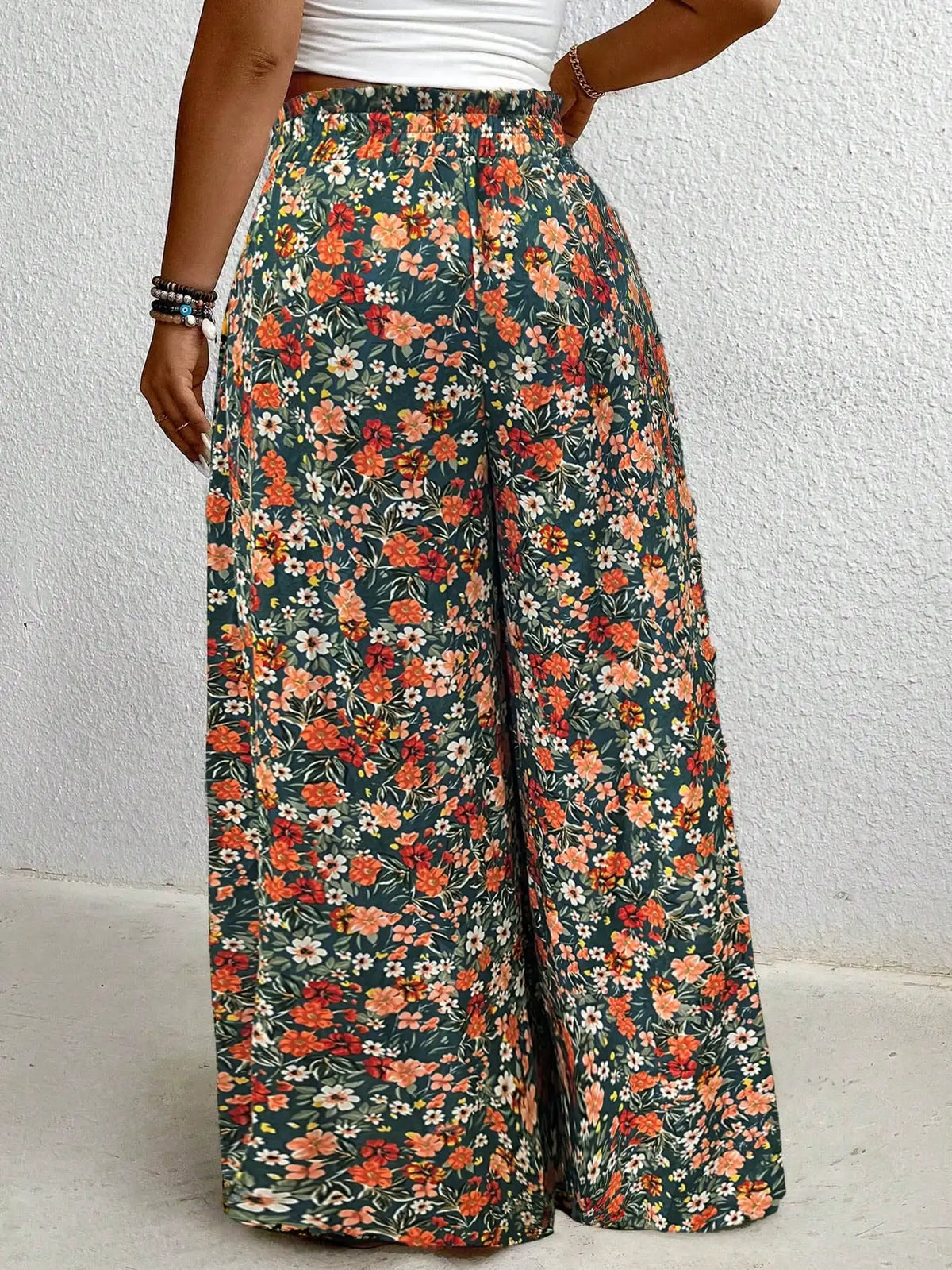 Back view of high waisted floral print wide leg pants with an elastic drawstring waist in green, orange, and white.