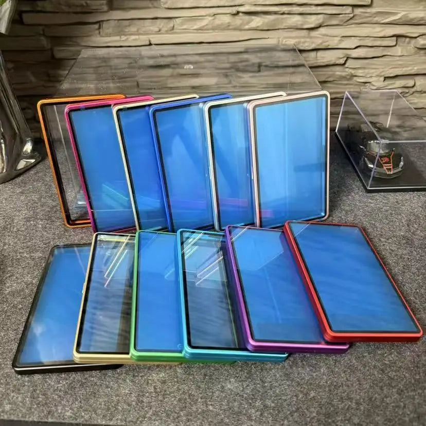 A collection of colorful metallic trading card cases with protective glass panels on a grey surface