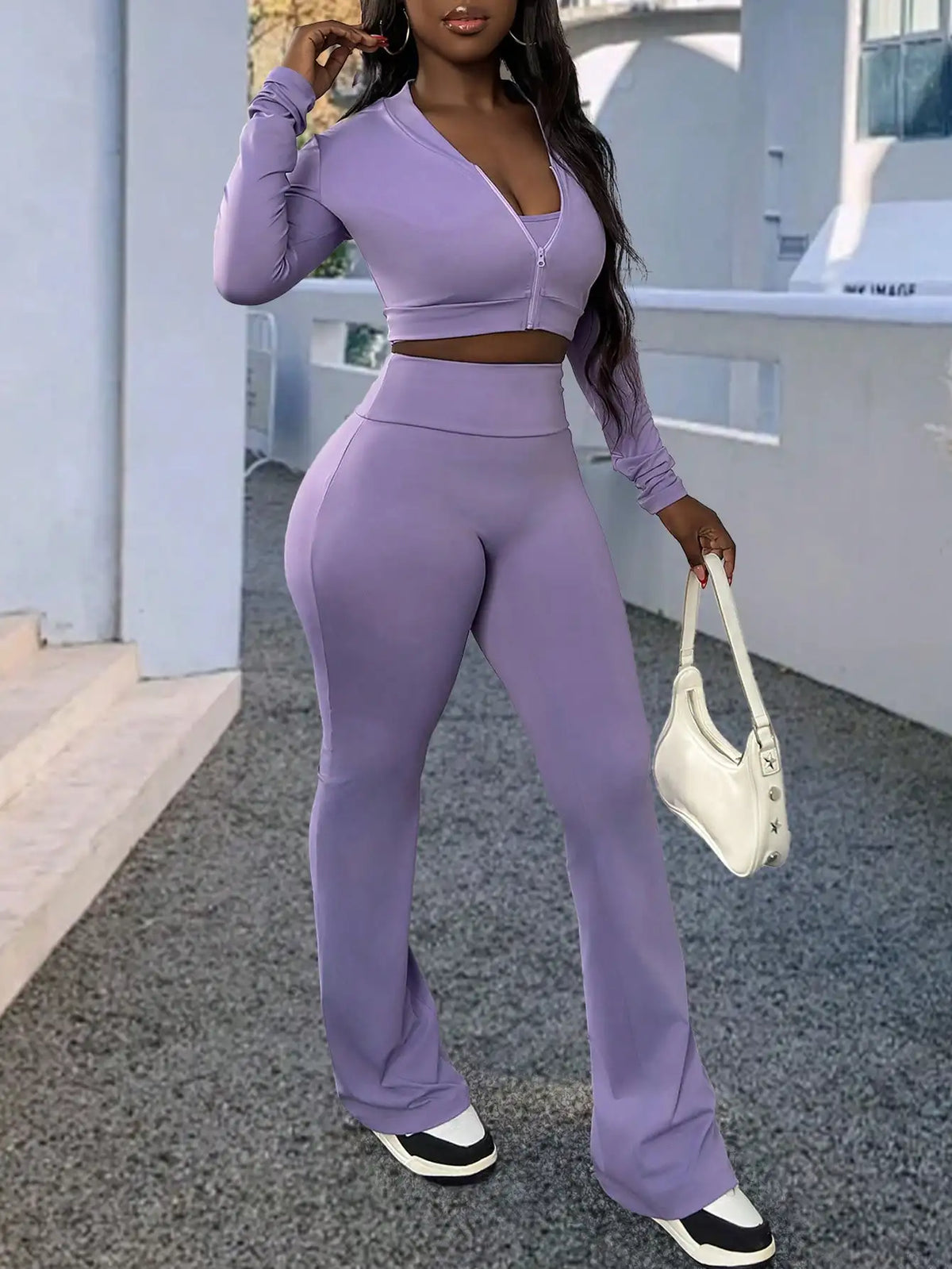 A woman wearing a purple long-sleeve zip-up top and matching flared trousers, carrying a white shoulder bag.
