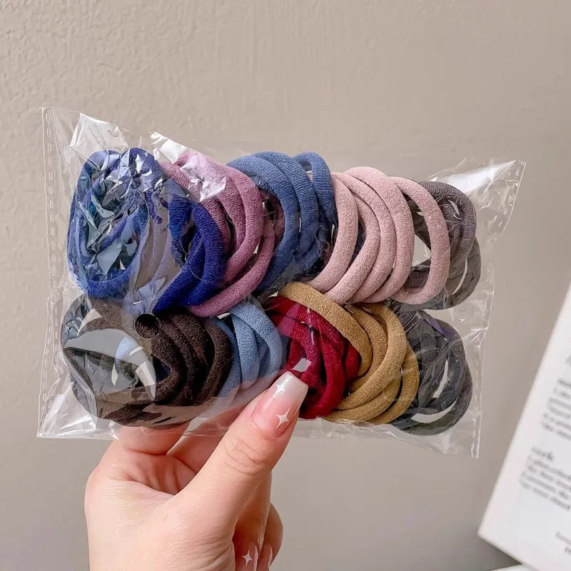 Hand holding a transparent plastic bag containing a variety of multicolored nylon hair ties.