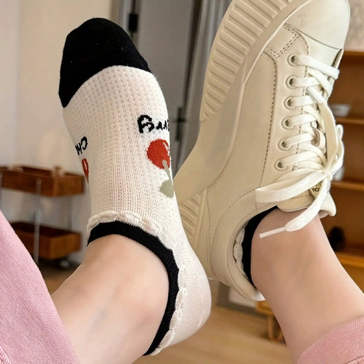 A person wearing a white cherry pattern ankle sock and a white sneaker
