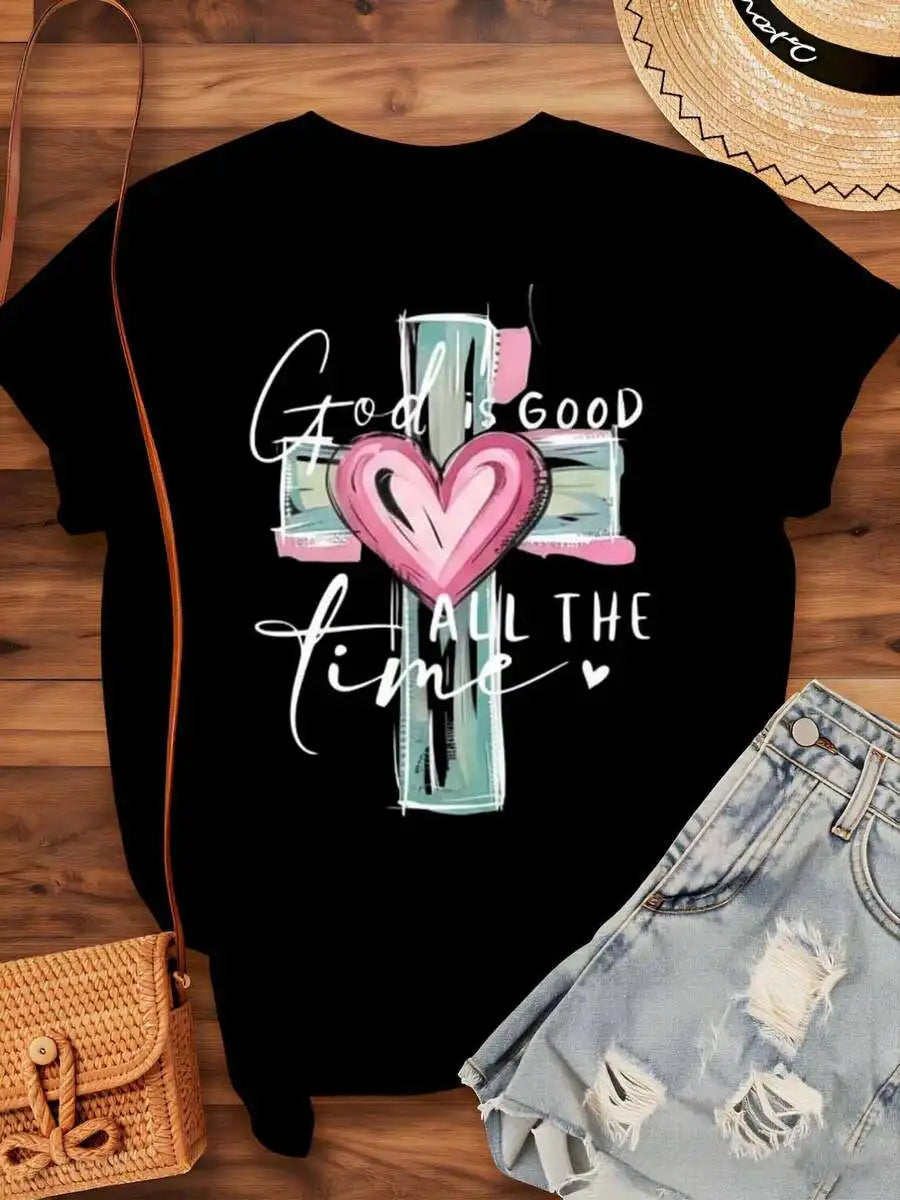 A black t-shirt with a religious cross and heart graphic print laid out on a wooden background.