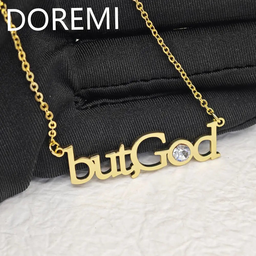 Gold necklace with the words butGod and a crystal on a black textured surface