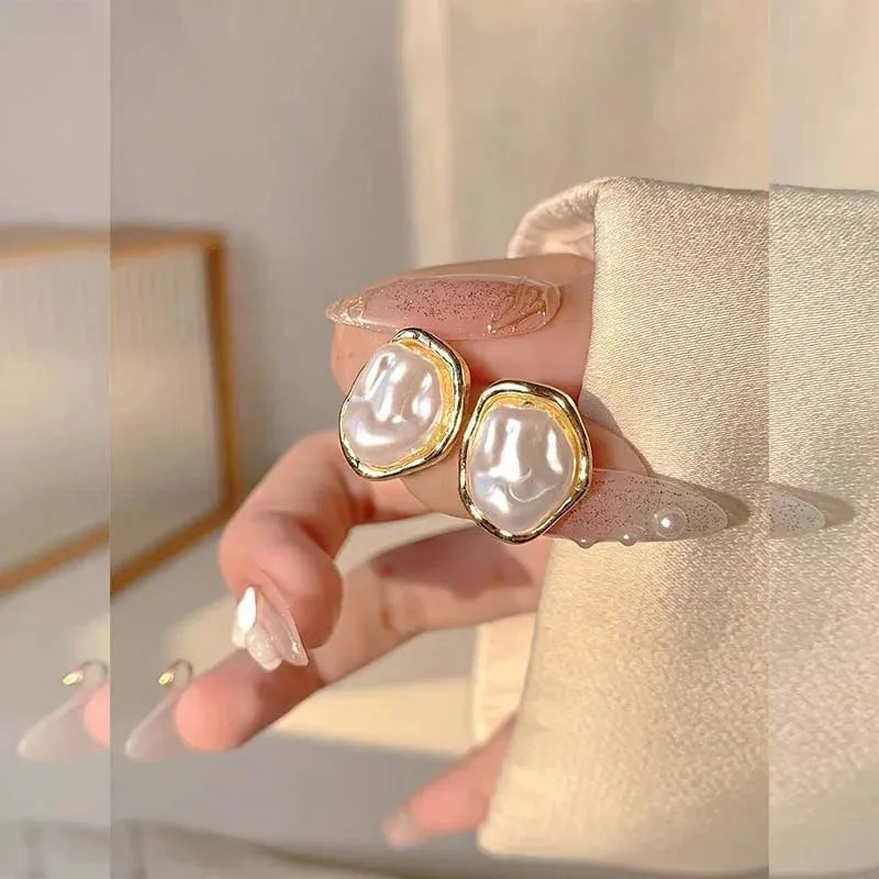Hand holding gold-rimmed irregular pearl earrings