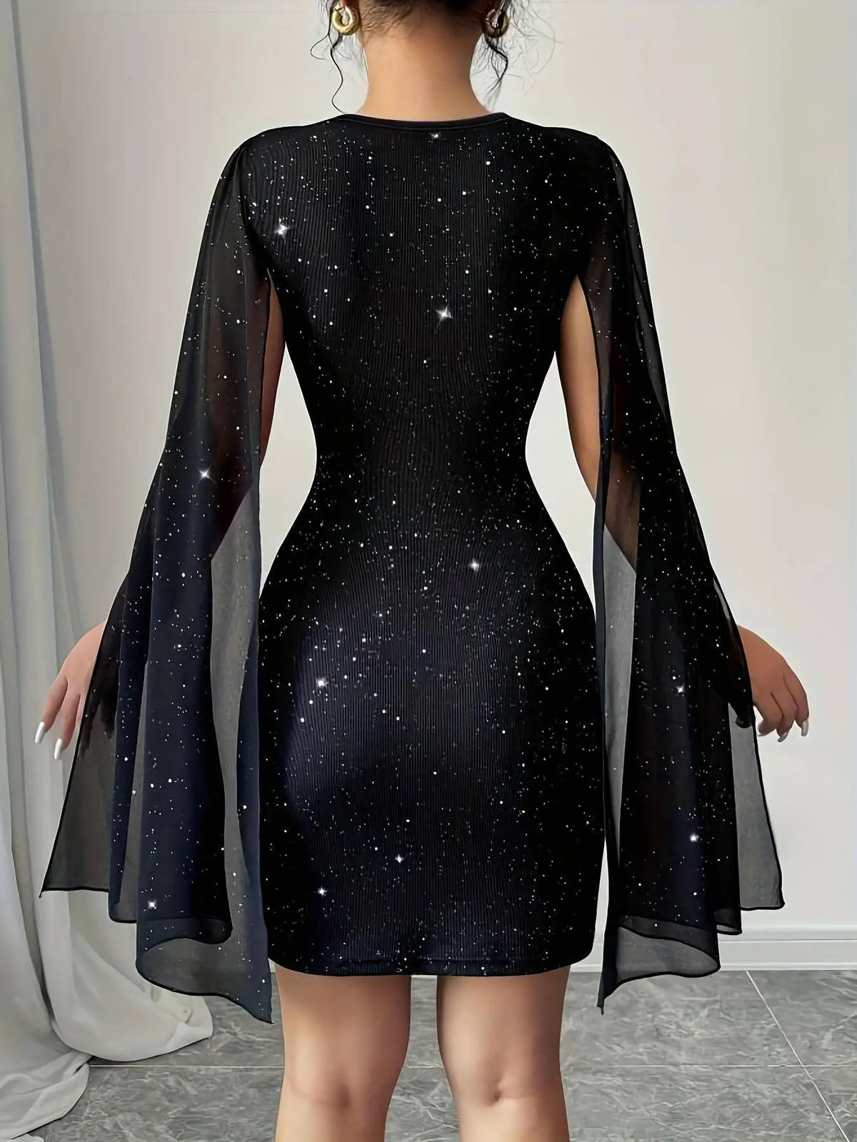 Back view of a black glittery bodycon mini dress with sheer cape sleeves