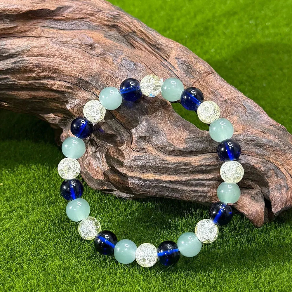 Beaded elastic bracelet with blue, light green and crackled clear beads resting on a piece of wood on green moss