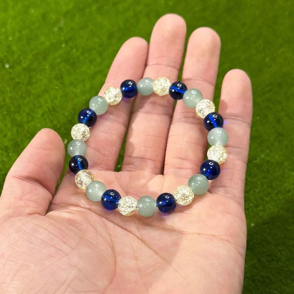 Beaded elastic bracelet with blue, light green and crackled clear beads held in a person's palm