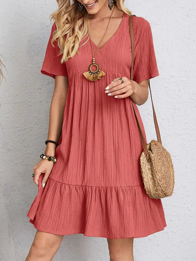 A woman wearing a short-sleeved coral-red V-neck textured mini dress with a tiered ruffle hem and a round straw crossbody