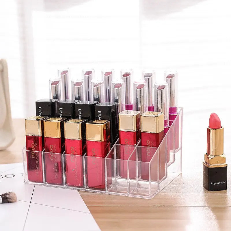 A clear acrylic lipstick storage organizer filled with red and black lipsticks on a desk