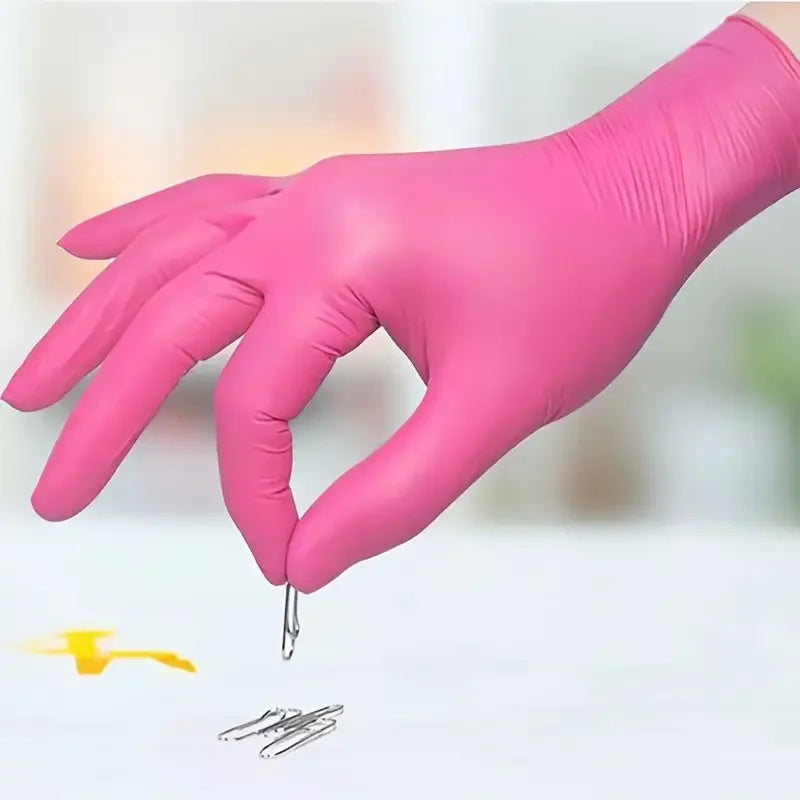 A hand wearing a pink nitrile glove picking up a small metal paperclip