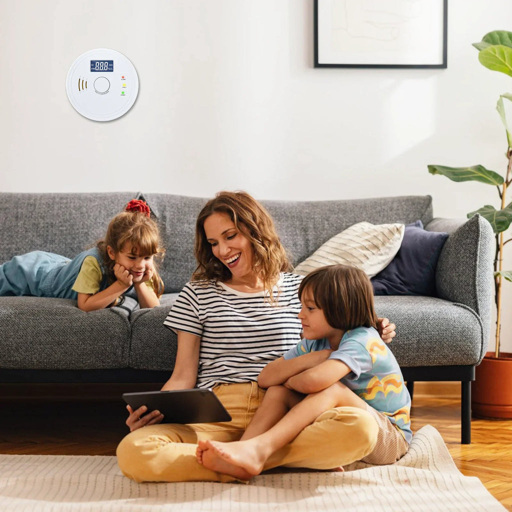 White smoke and carbon monoxide detector mounted on a living room wall with a family sitting on a sofa