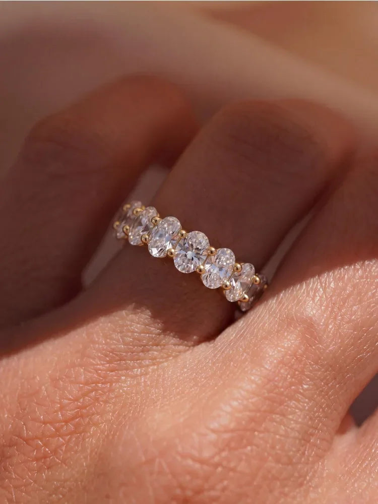 Eternity band ring featuring oval-cut white zircon stones set in gold-plated sterling silver, worn on a finger.