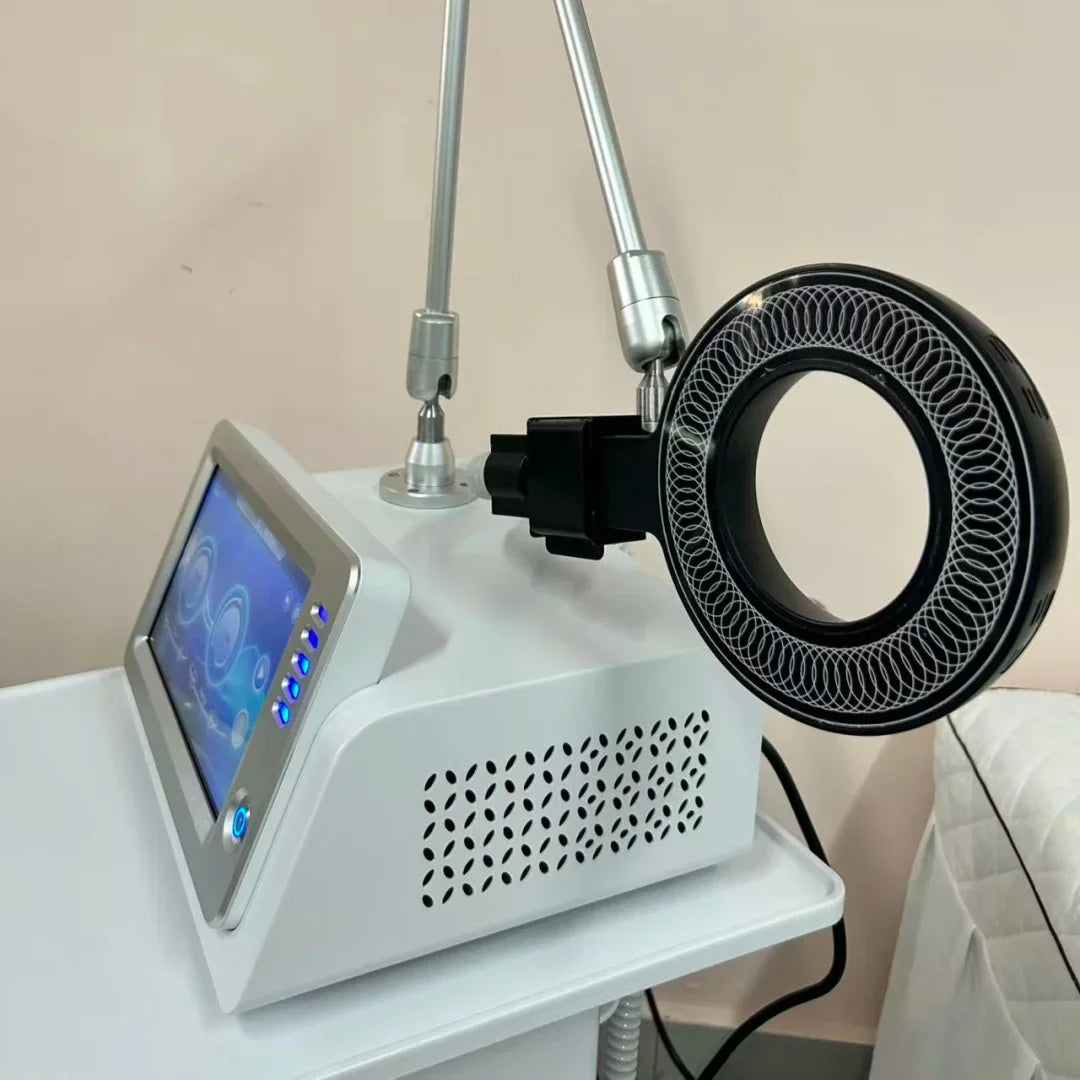 A white physical therapy machine with a touchscreen and a black magnetic ring applicator on a white table
