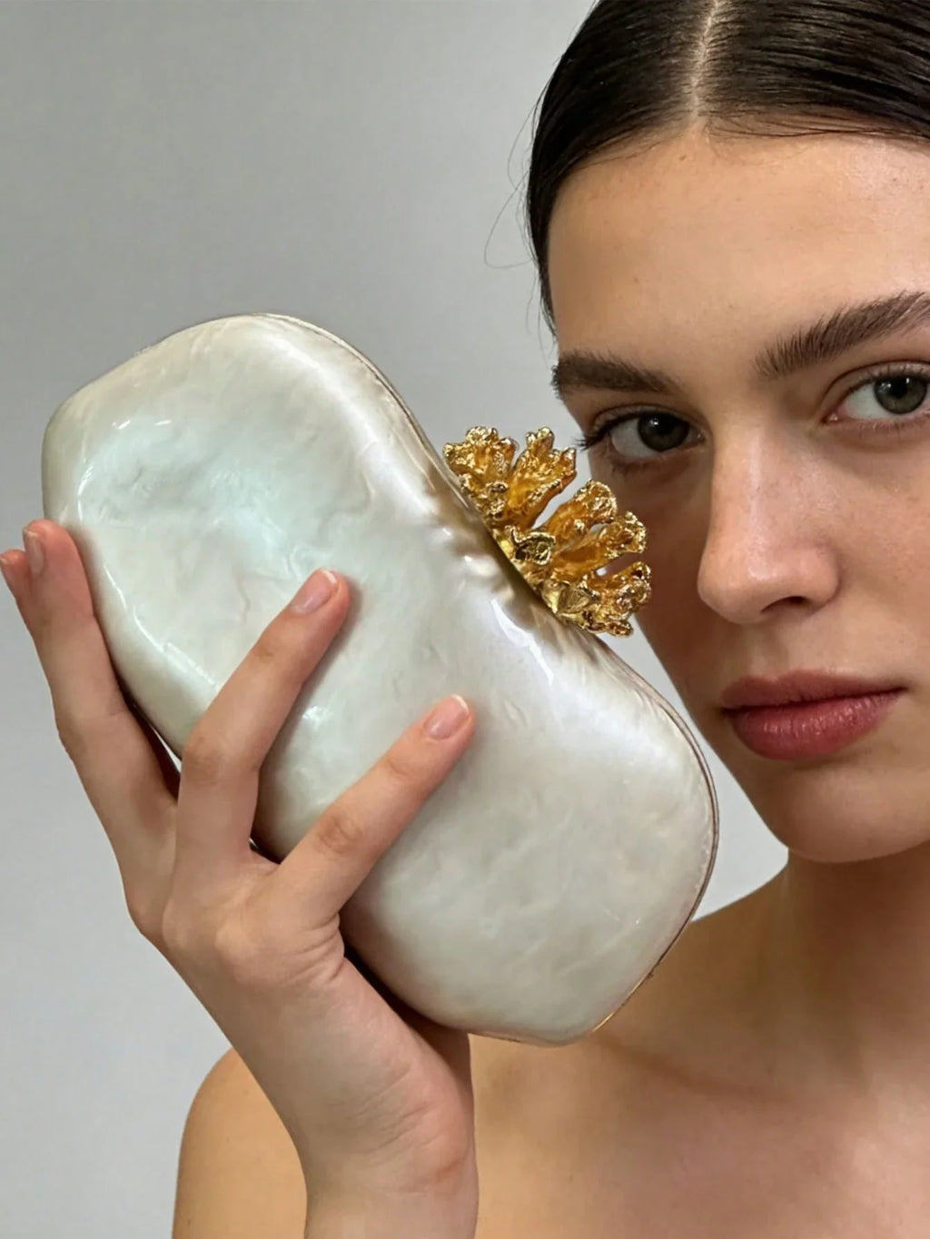 White marbled acrylic evening clutch with gold coral-shaped clasp held by a woman