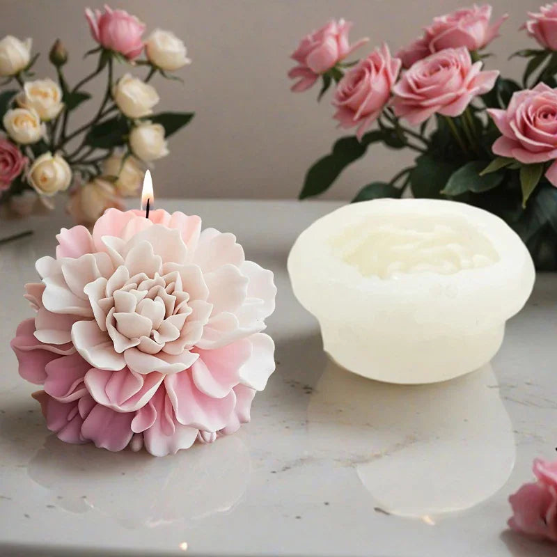 A lit pink peony shaped flower candle next to a white silicone mold