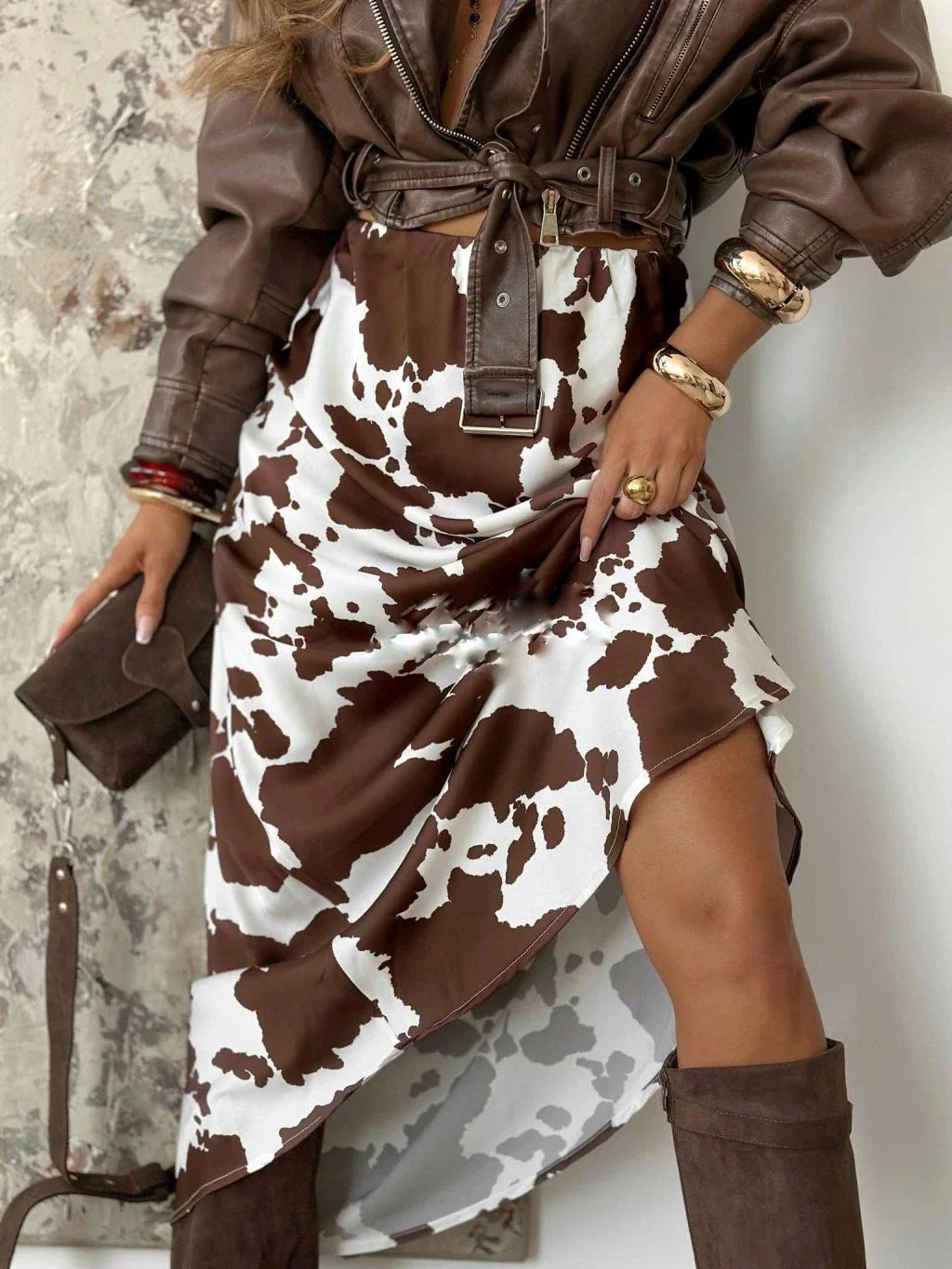 A high-waisted midi skirt with a brown and white cow print pattern worn with a leather jacket