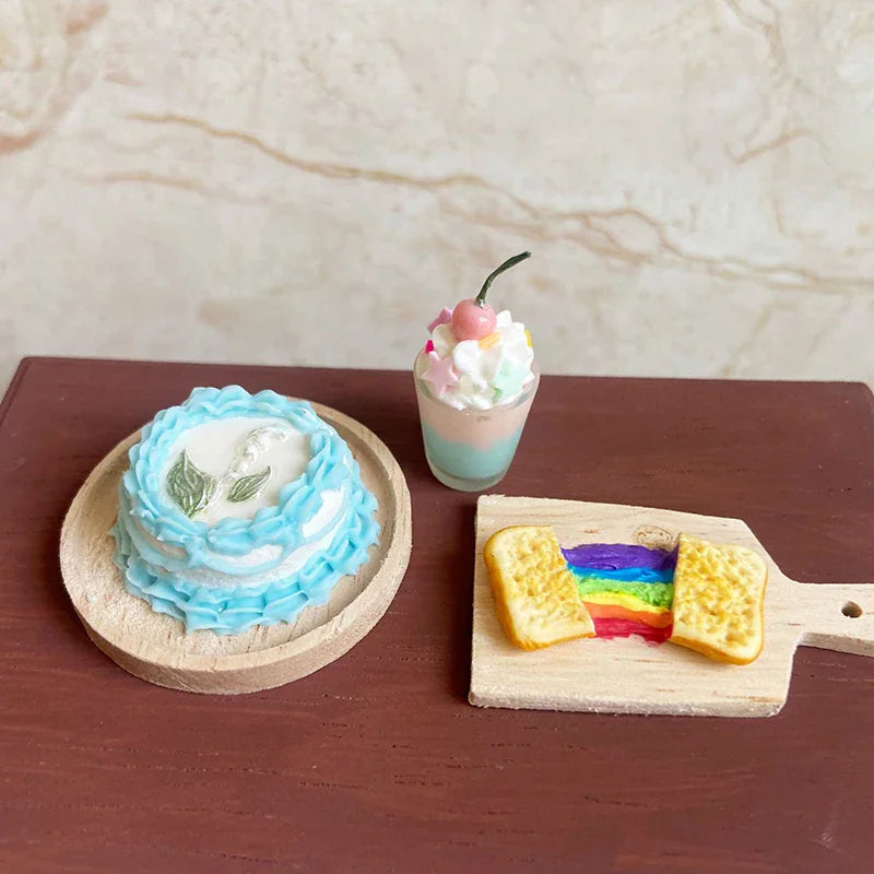 Miniature blue frosted cake with a lily, a small sundae with cherry, and rainbow toast on a wooden board.