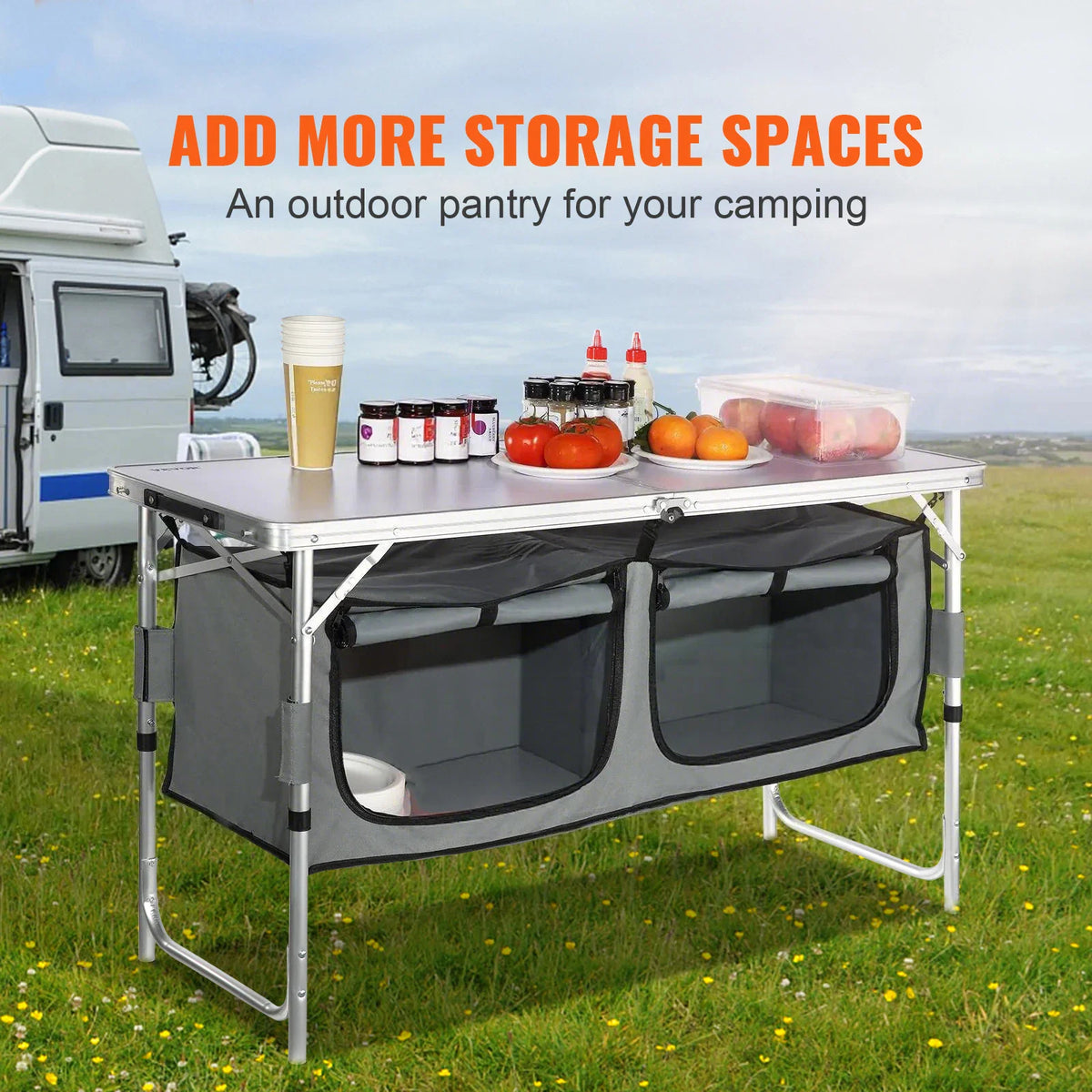 Outdoor camping table with fabric storage shelves set up on a grass field near a camper van