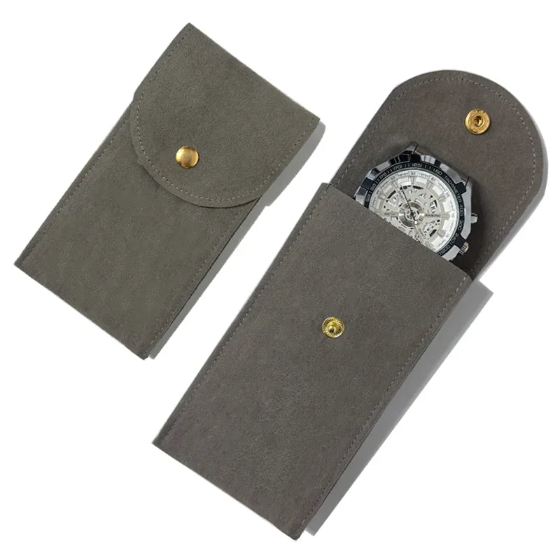 A gray suede watch storage pouch with a snap button and a skeleton watch.