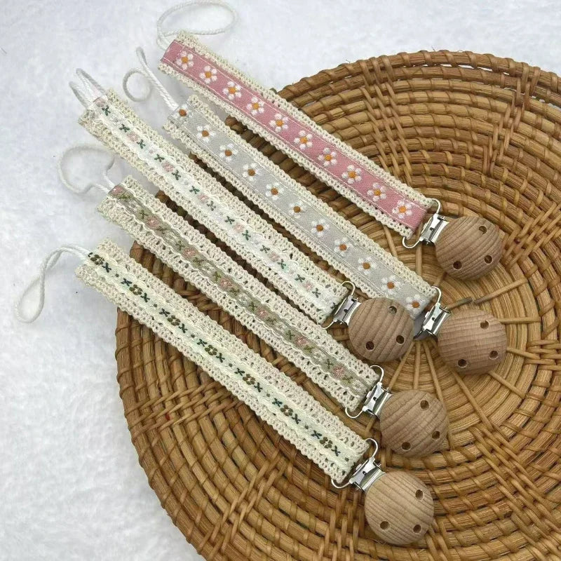 A set of fabric pacifier chains with floral patterns and wooden clips on a woven tray.