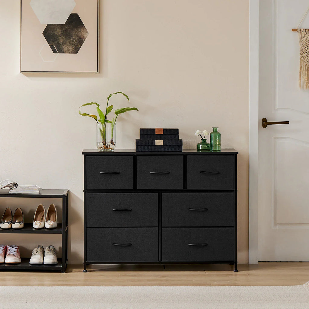 A black seven-drawer fabric dresser with a sturdy metal frame in an entryway with shoes and plants.