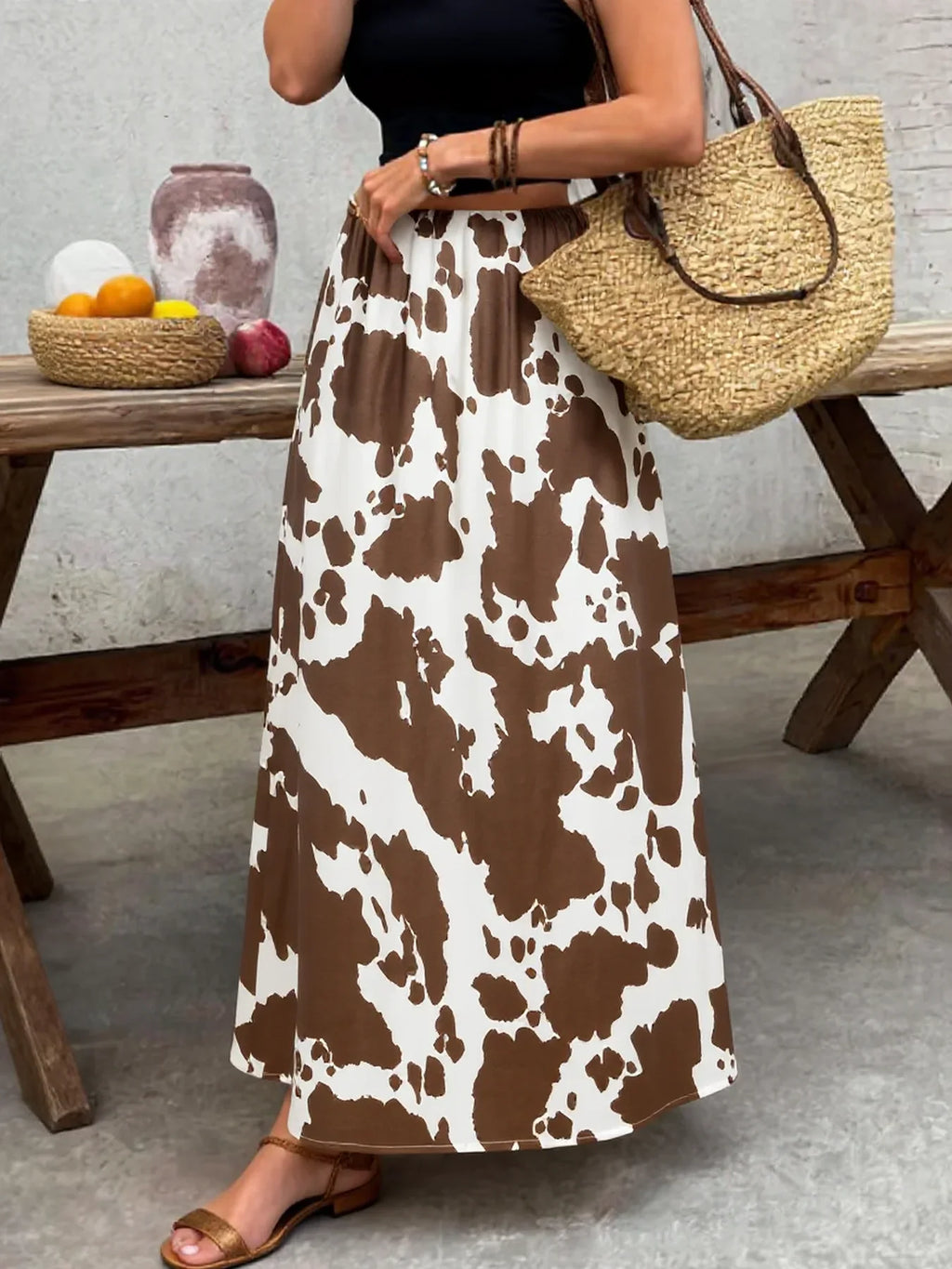 A high-waisted A-line midi skirt with a brown and white cow print pattern worn with a straw bag