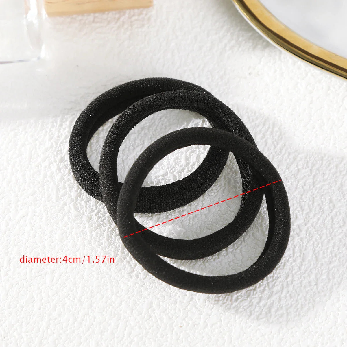 Three black elastic hair ties on a textured white surface with a diameter measurement label.