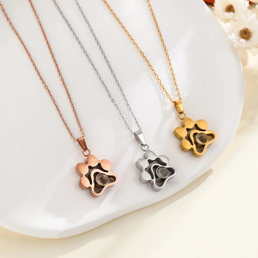 Set of three stainless steel paw-shaped projection necklaces in rose gold, silver, and gold on a white surface.