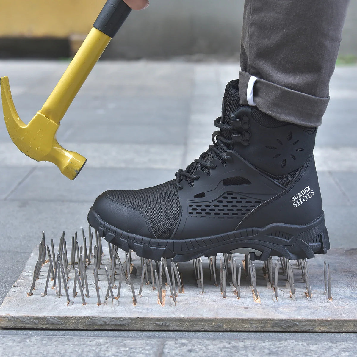 Person wearing black safety boots stepping on sharp nails, holding a hammer
