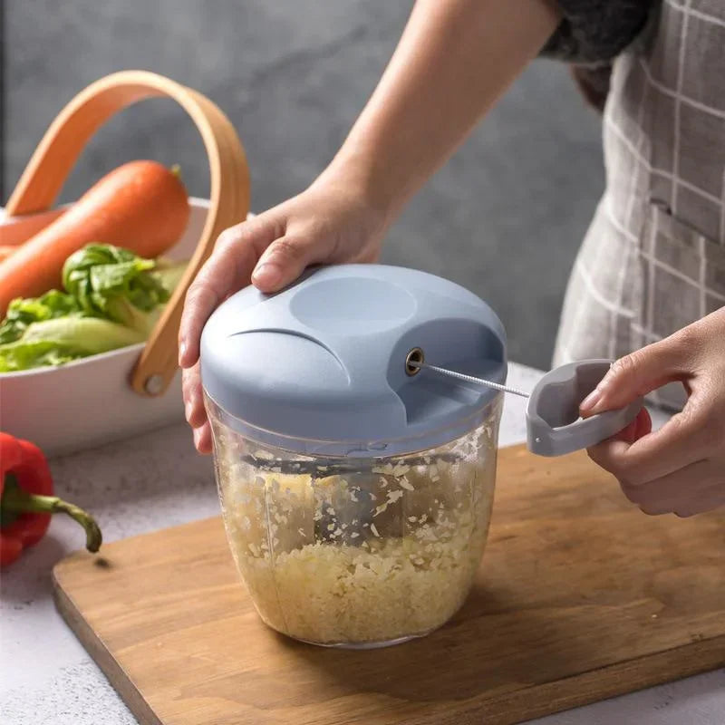 A person using a hand-pulled vegetable chopper to mince garlic on a wooden cutting board.