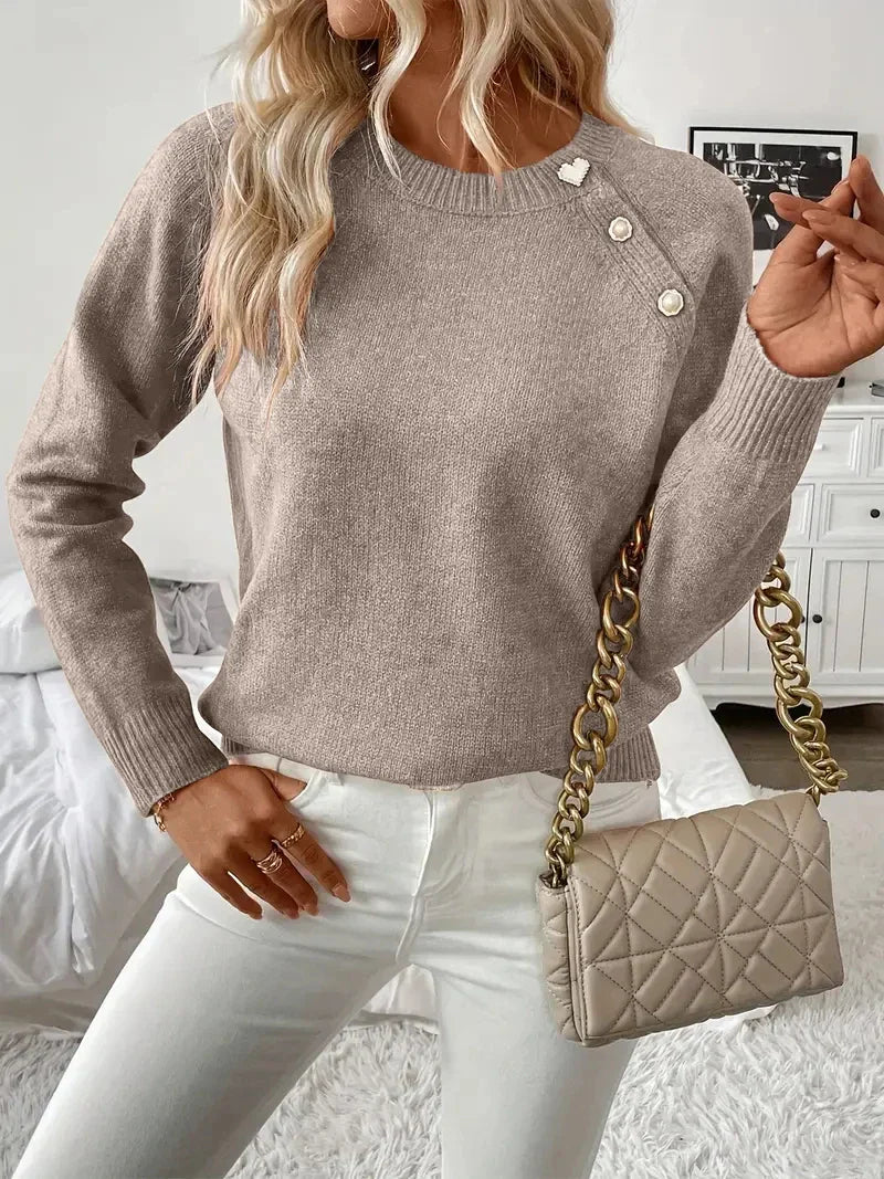 Woman wearing a taupe long-sleeve knit sweater with button detail at the shoulder