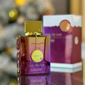 Gradient purple and orange perfume bottle with a gold square cap and a hanging charm on a blurry background