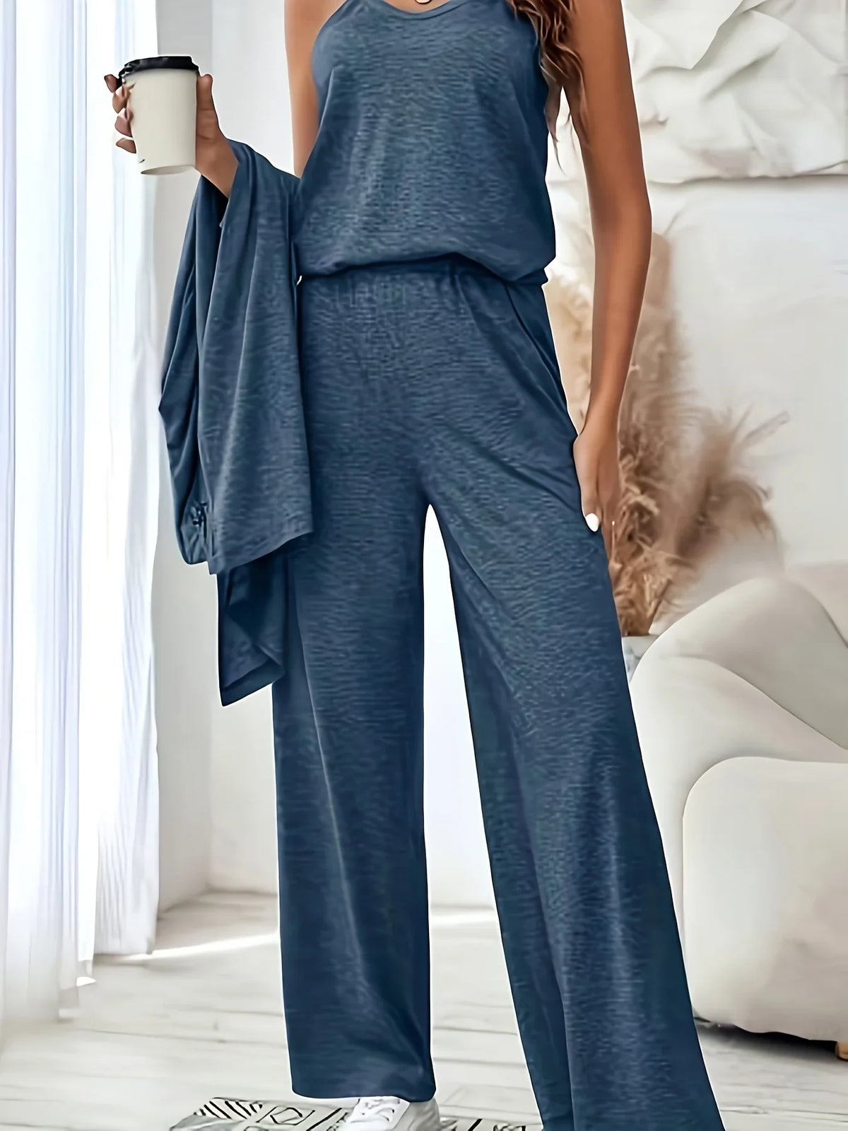 A woman wearing a blue three-piece loungewear set holding a cup of coffee, showcasing the tank top and wide-leg pants