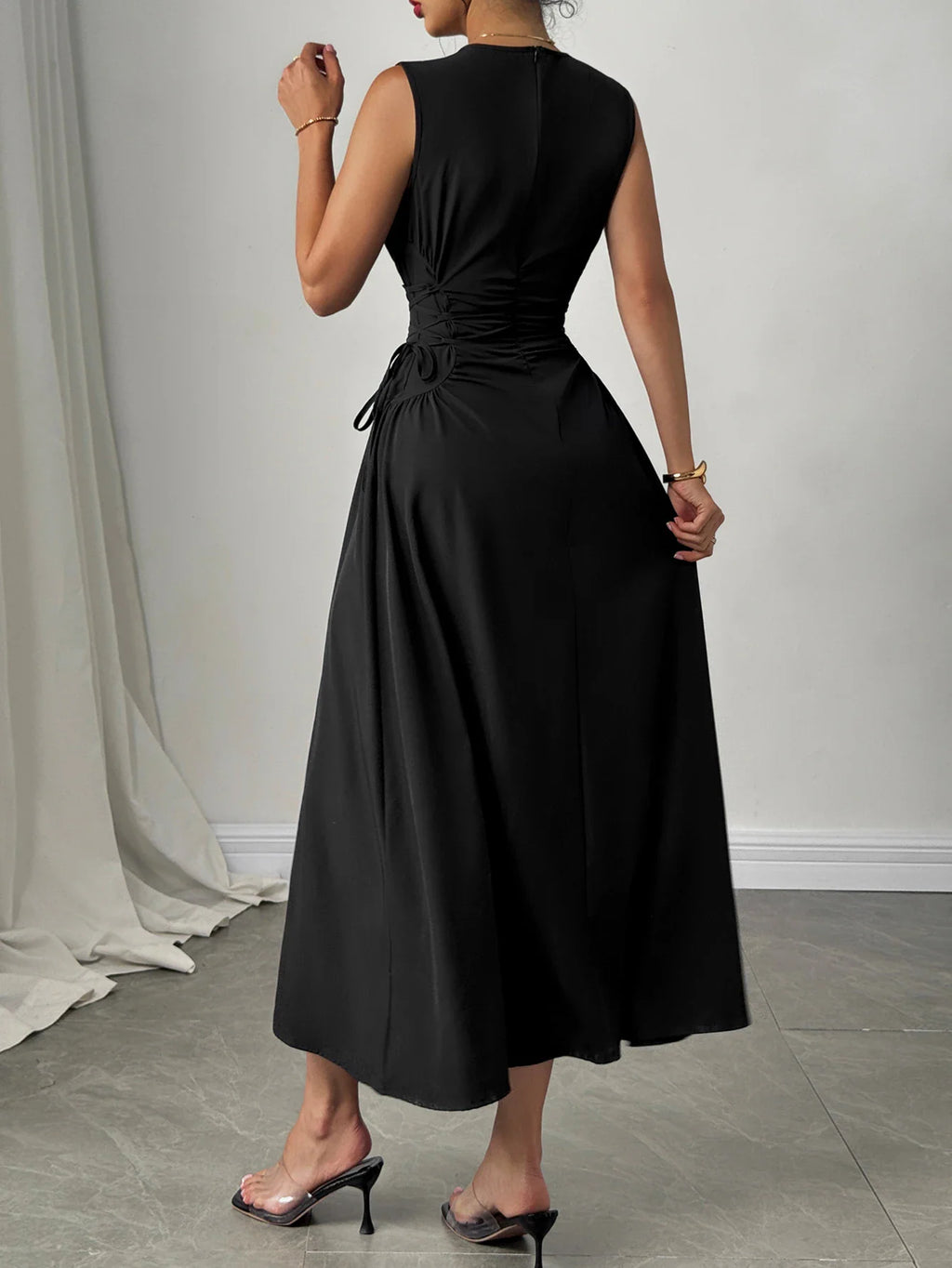 Back view of a woman wearing a black sleeveless midi dress with cinched waist detailing.