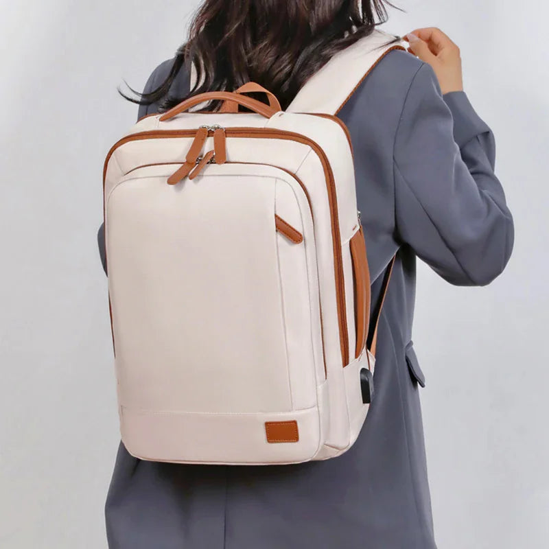 A person wearing a beige laptop backpack with brown accents against a neutral background.