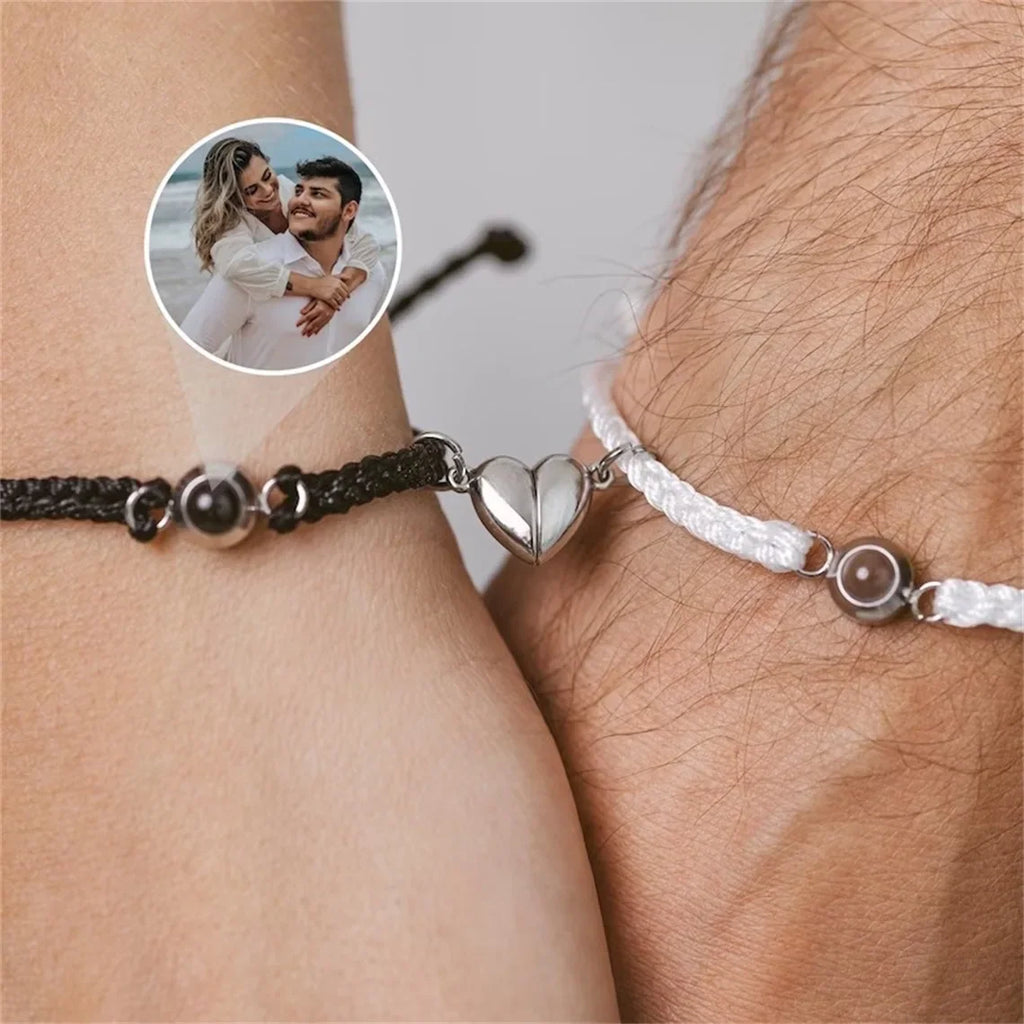 Couple wearing black and white braided magnetic heart bracelets featuring a photo projection charm