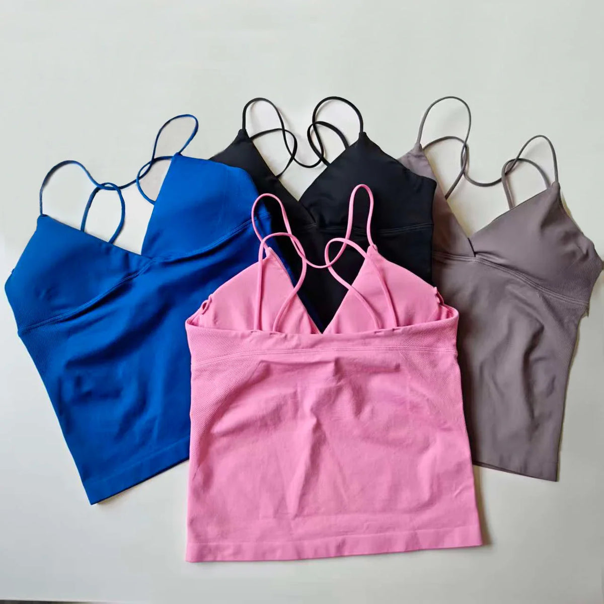 A group of seamless workout tank tops in pink, blue, black, and grey with thin straps.