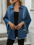 A woman wearing a loose-fit, blue denim jacket with a frayed hem and cloak design, over a black top