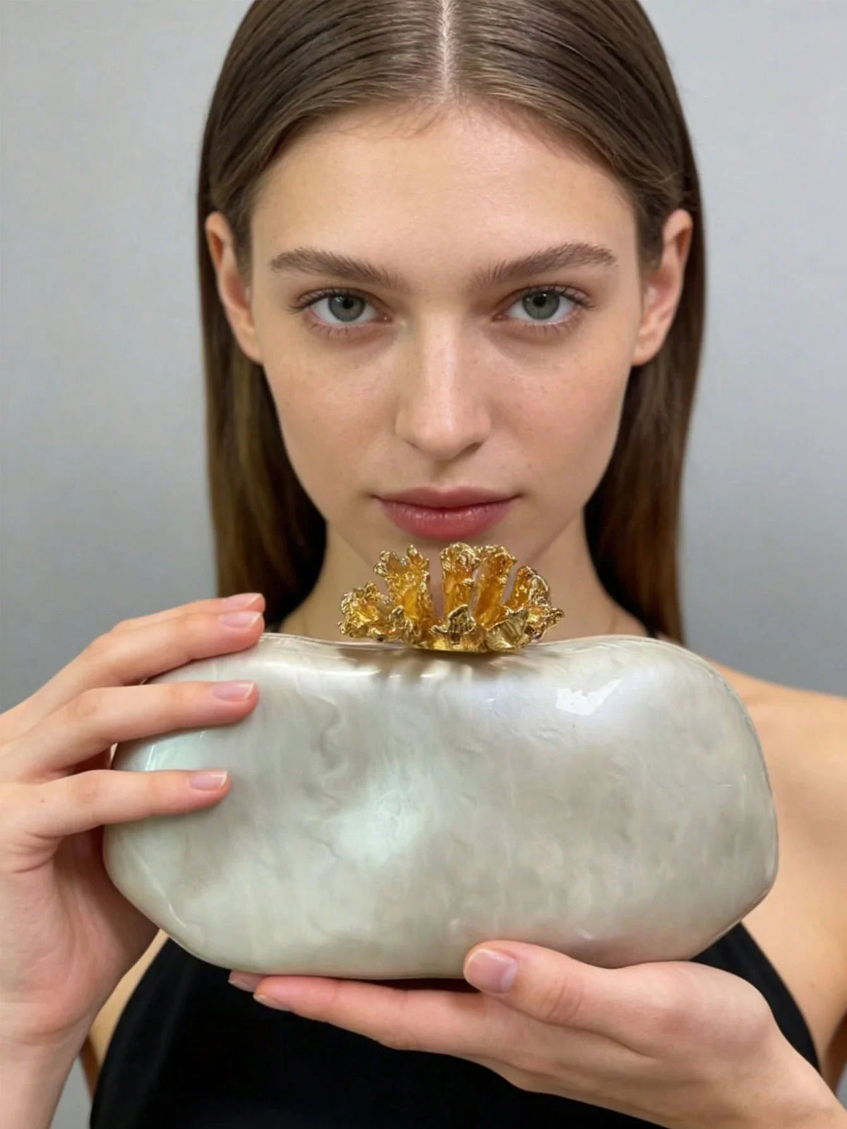 White marbled acrylic evening clutch with gold coral-shaped clasp held by a woman
