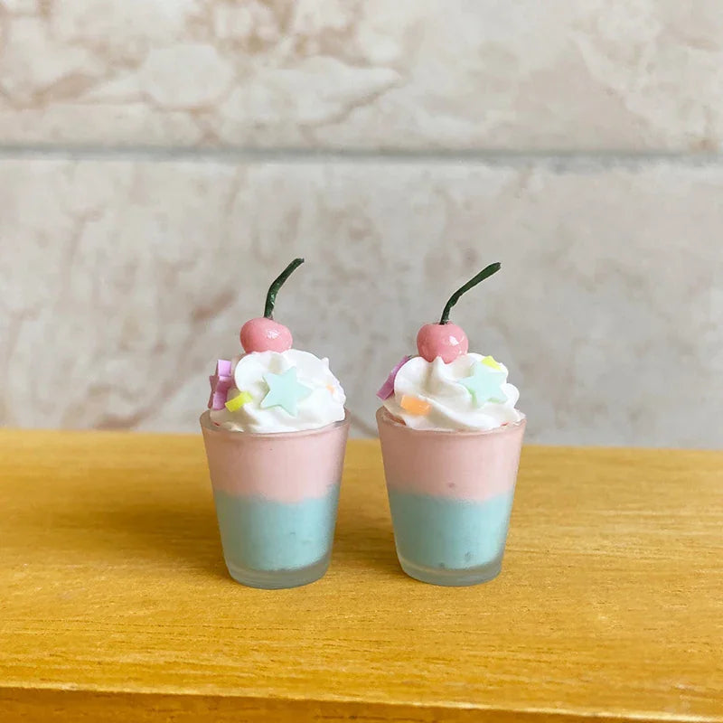 Two miniature dessert cups with pink and blue layers, whipped cream, star sprinkles, and cherry toppers.