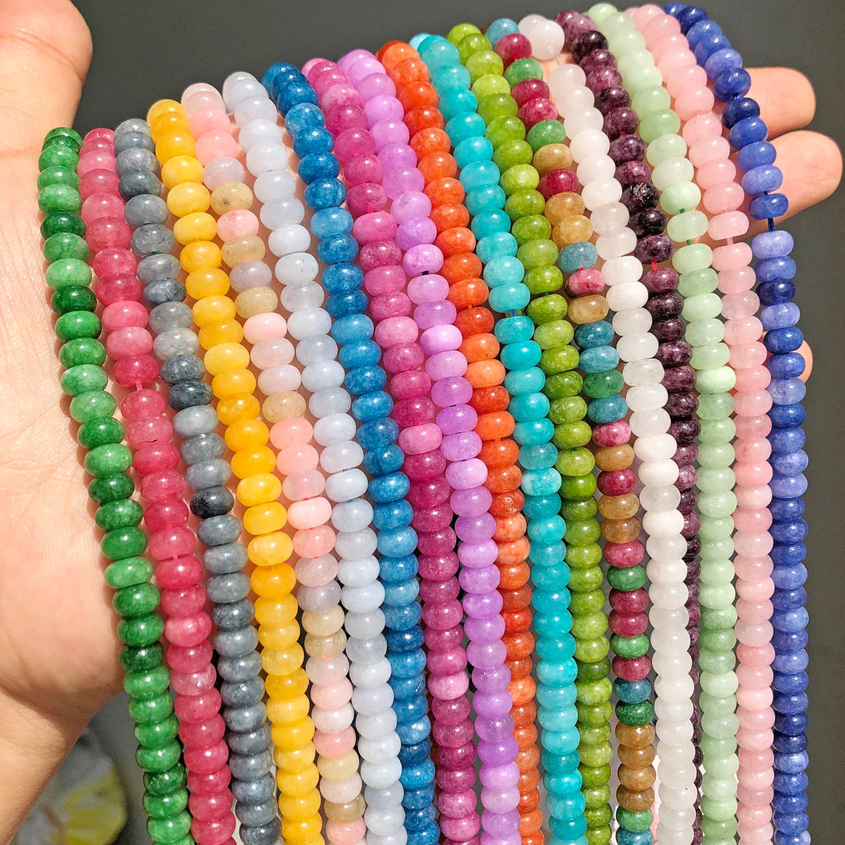 Hand holding strands of colorful natural gemstone abacus rondelle beads for jewelry making