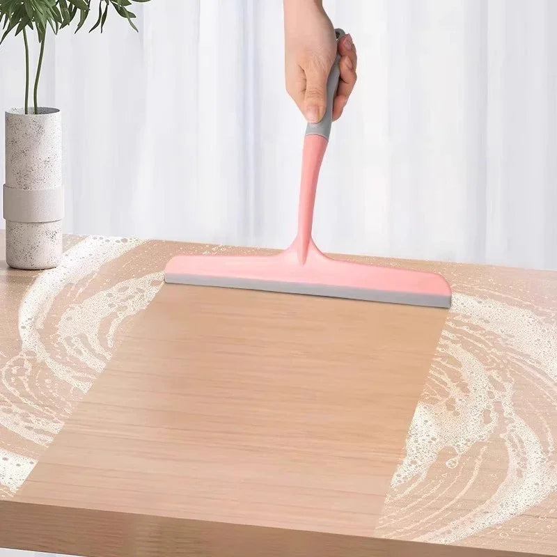 Hand holding a pink silicone squeegee cleaning a soapy wooden surface