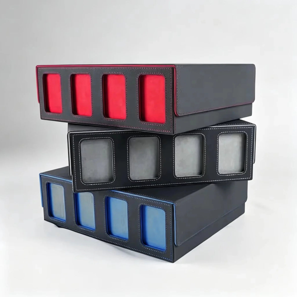 A stack of three trading card storage boxes with red, grey, and blue interior linings.