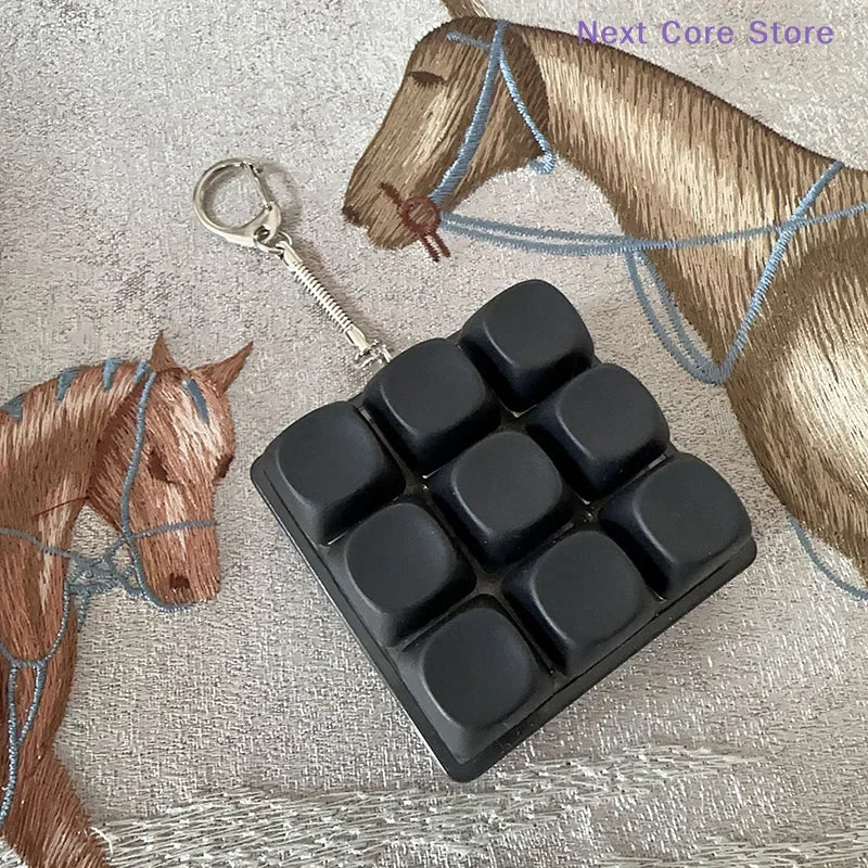 A black 9-key keyboard fidget keychain resting on a fabric with a horse pattern