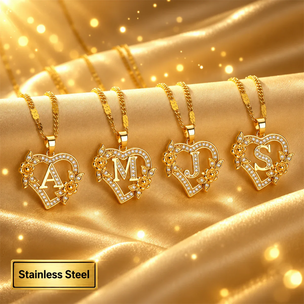 Four gold heart-shaped initial necklaces with floral accents on a shiny fabric background