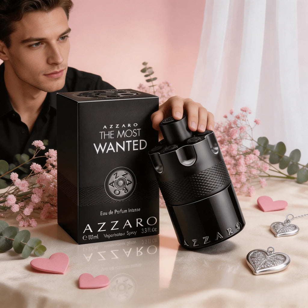 A man's hand holding an Azzaro The Most Wanted fragrance bottle with the product box, roses, and hearts