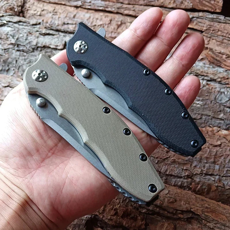 Hand holding two closed folding pocket knives with black and tan handles against a wooden background