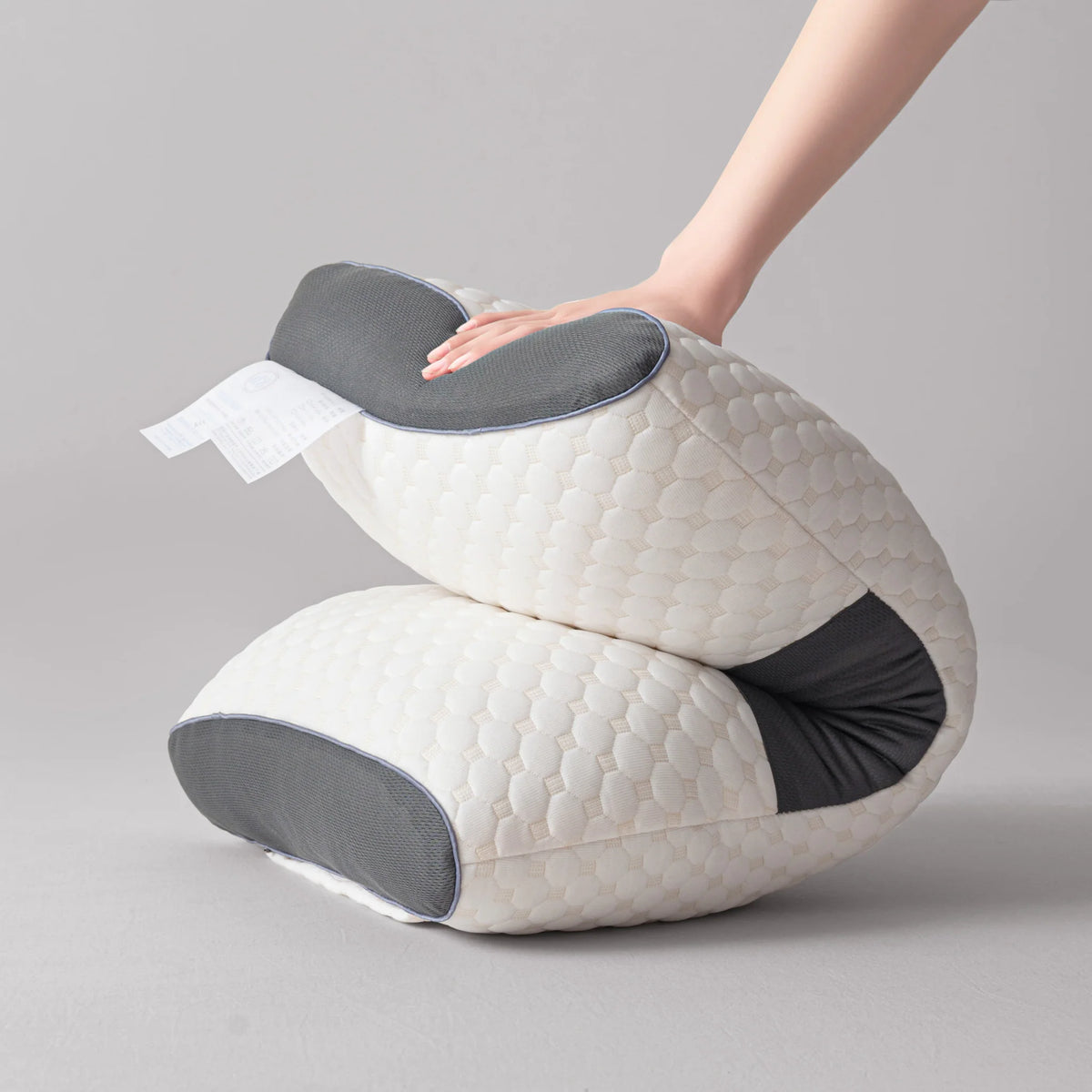 Hand pressing on a flexible white and grey ergonomic orthopedic contour pillow