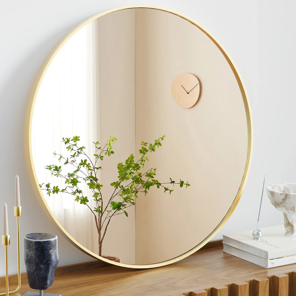 A large round mirror with a gold frame displayed on a wooden surface with decorative items