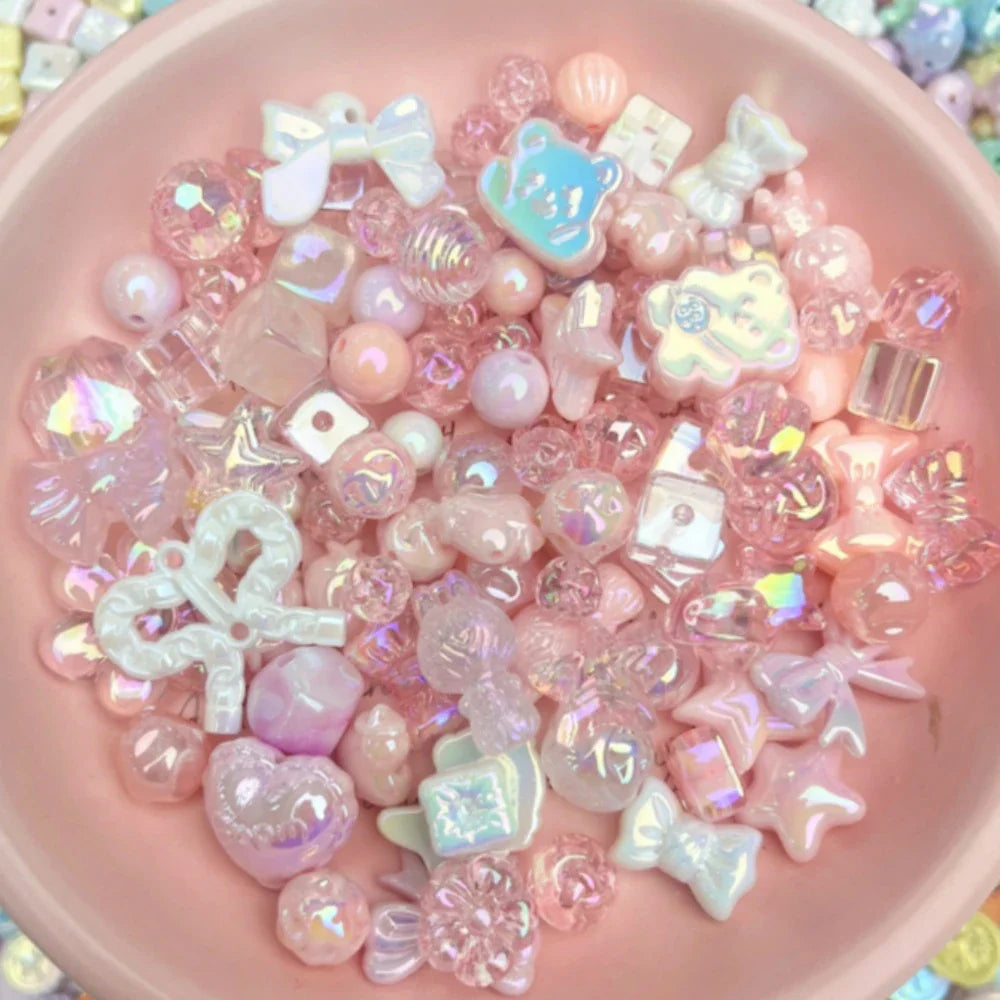 A pink bowl filled with an assortment of iridescent pink, white, and clear craft beads in shapes like bows, hearts, and